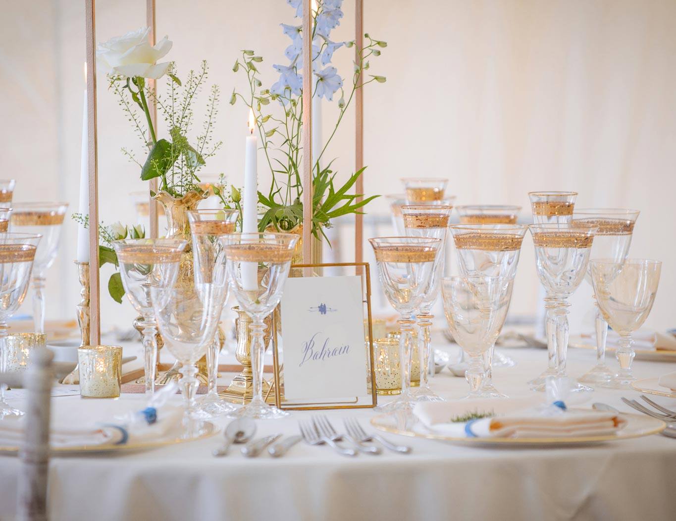 Elegant table setting with floral centerpiece, glassware, and place cards. Gold accents, white tablecloth.