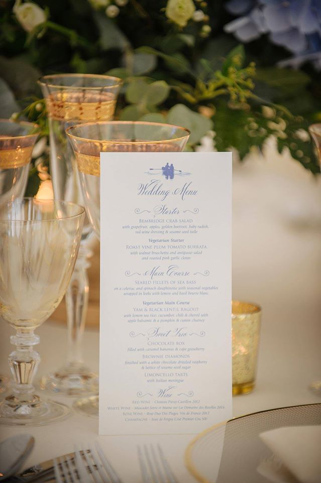 Wedding menu on a table, with glasses, gold accents, and floral centerpiece in a well-lit setting.