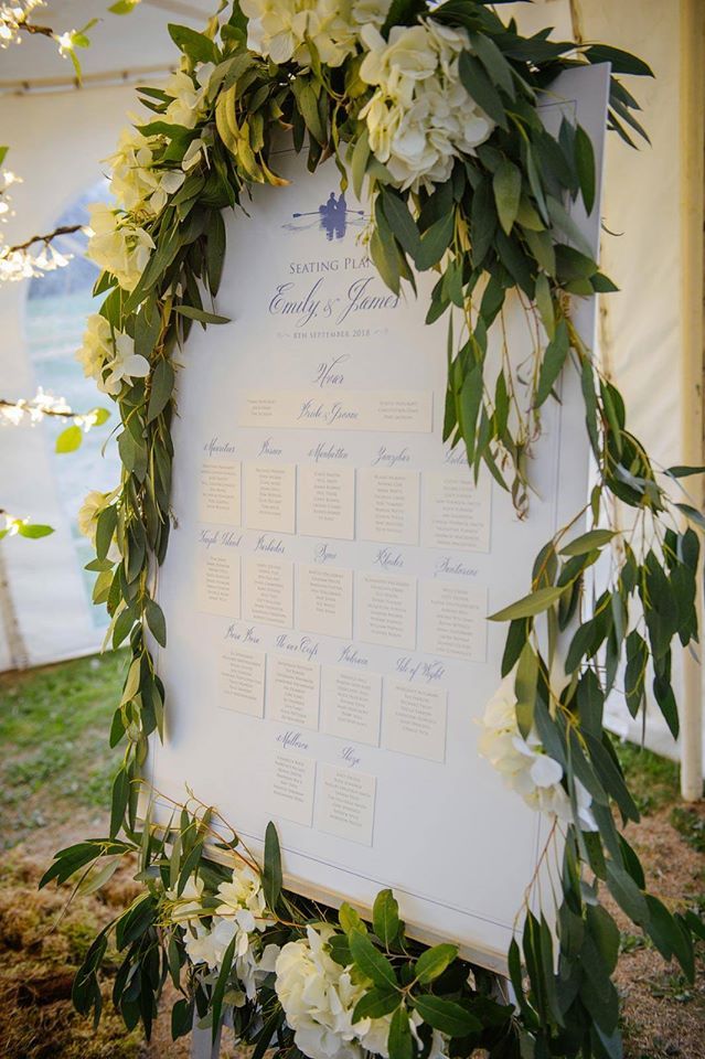 Wedding seating chart decorated with greenery and white flowers.