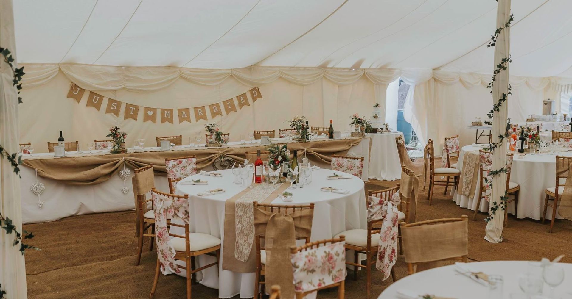 Wedding reception tent interior with decorated tables, chairs, and bunting.