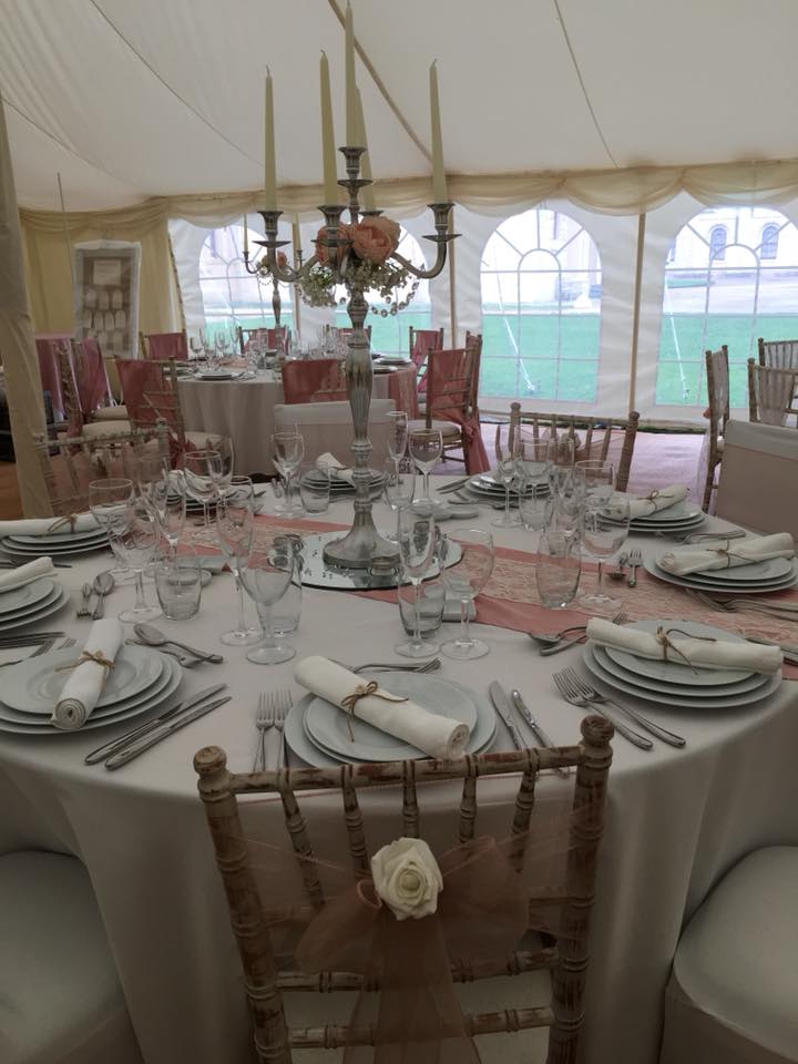 Elegant round dining table set for a wedding, in a white tent, with floral centerpiece and place settings.