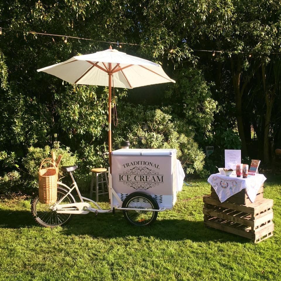 Ice cream cart with an umbrella, on a lawn with a table display.