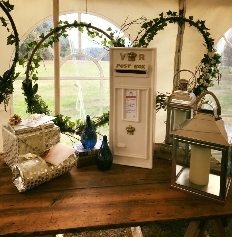 Wooden table with a white post box and two lanterns, decorated with vines.