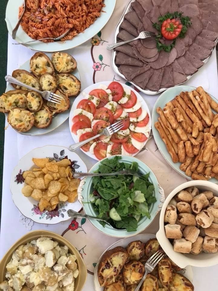 A table spread with various foods: pasta, sliced meats, tomatoes and mozzarella, potatoes, and salad.