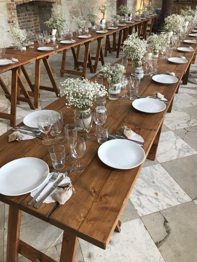 Long wooden tables set for a meal, with white plates, glassware, and floral centerpieces.