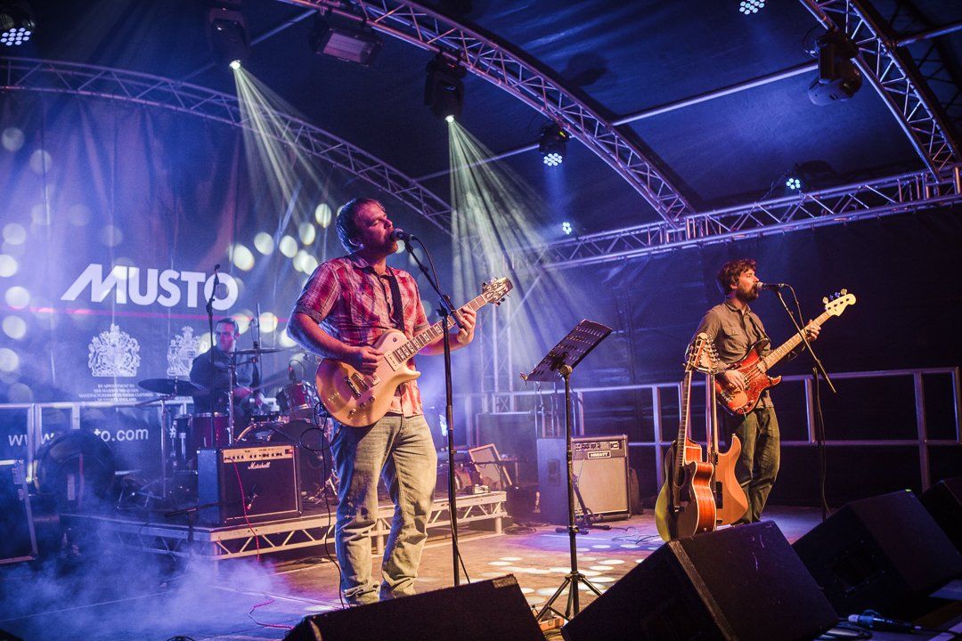 Band performing on stage under stage lights, including guitarist and bassist.