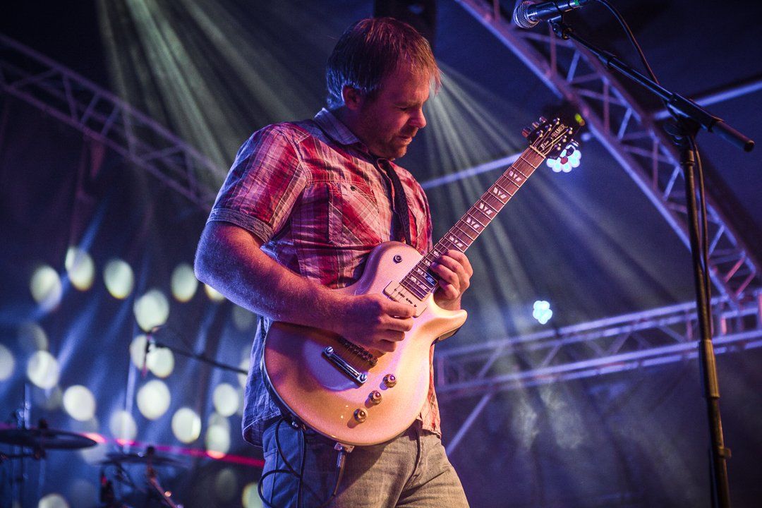 Guitarist playing onstage under stage lights.