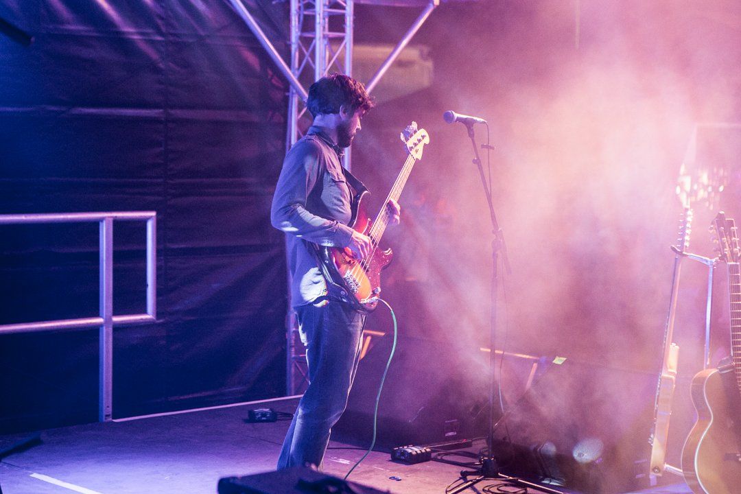 Man playing electric bass guitar on stage, bathed in blue and purple stage lighting and smoke.