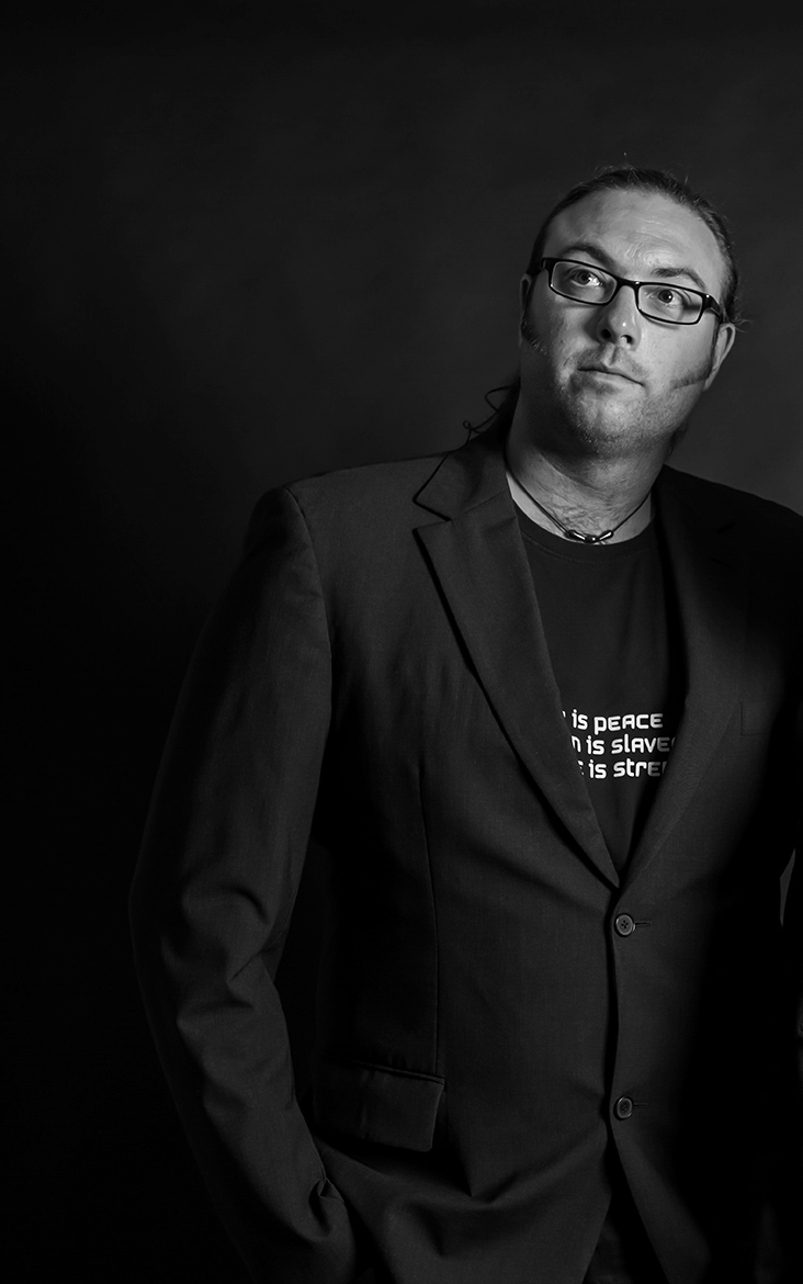 Man in glasses and suit jacket, looking slightly up and to the right, against a dark background.