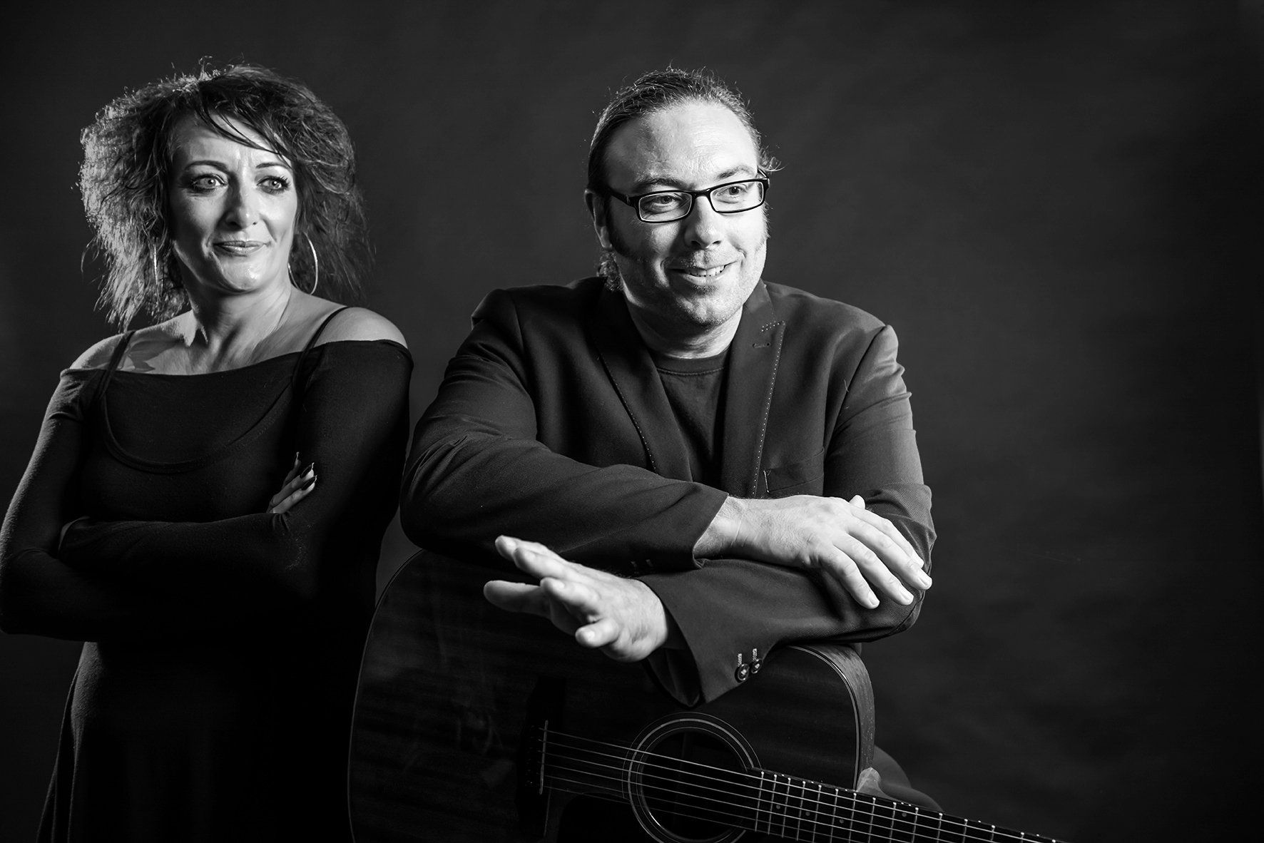 Two people, a woman and a man, posing for a portrait in black and white; man with guitar, both smiling.