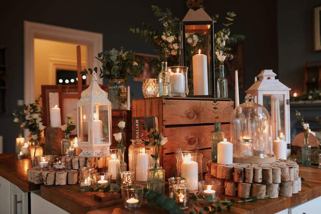 Wooden table decorated with candles, lanterns, flowers, and wooden crates for an event.