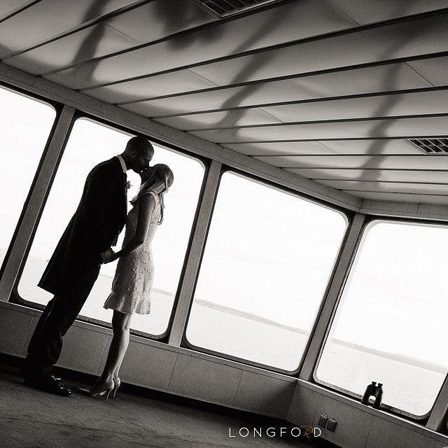 Couple embraces, kissing near large windows. Aboard a ship, black and white photo.