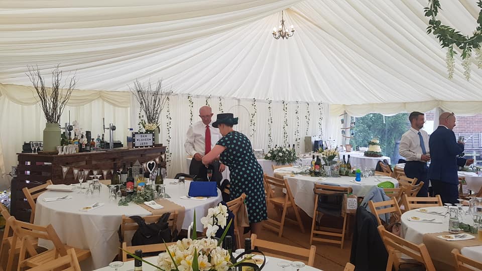 Wedding reception inside a tent, with round tables, decorations, and people interacting.