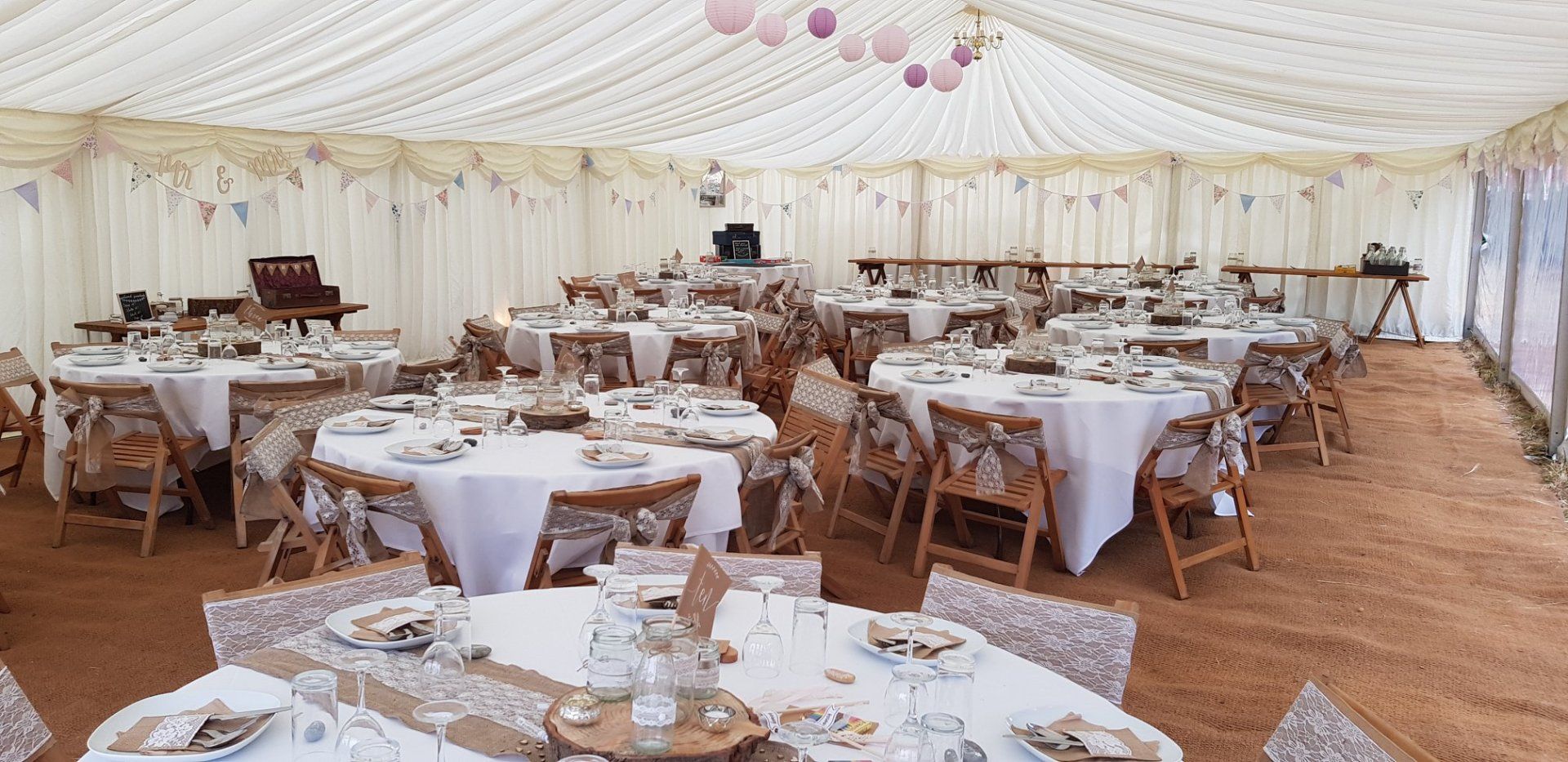 Wedding reception tent with round tables set with white linens, chairs, and decorations.