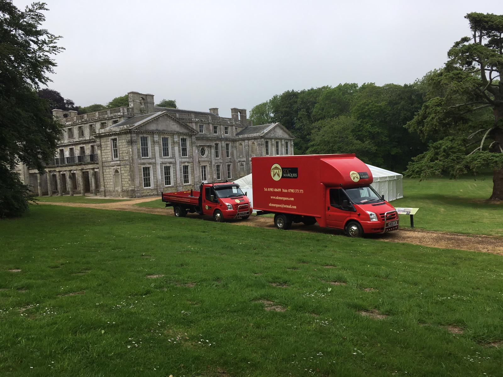 Two red trucks parked on a lawn in front of a large, decaying stone building.
