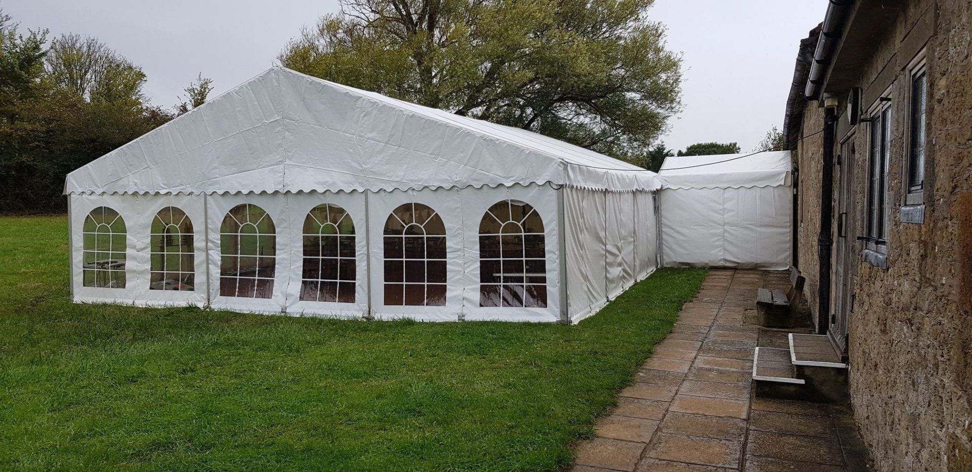 A white tent attached to a stone building with arched windows, set on a green lawn.