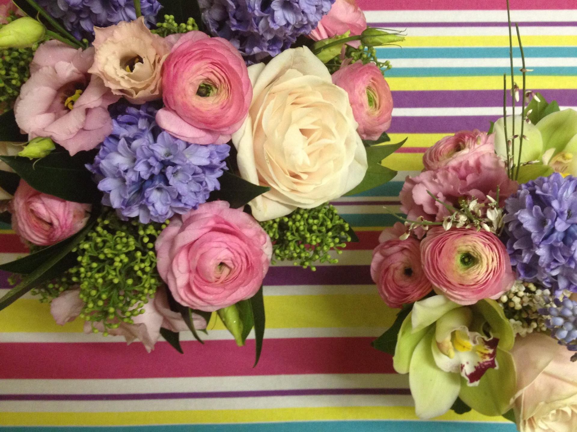 Bouquet of colorful flowers, including pink ranunculus, hyacinths, and orchids, on striped background.