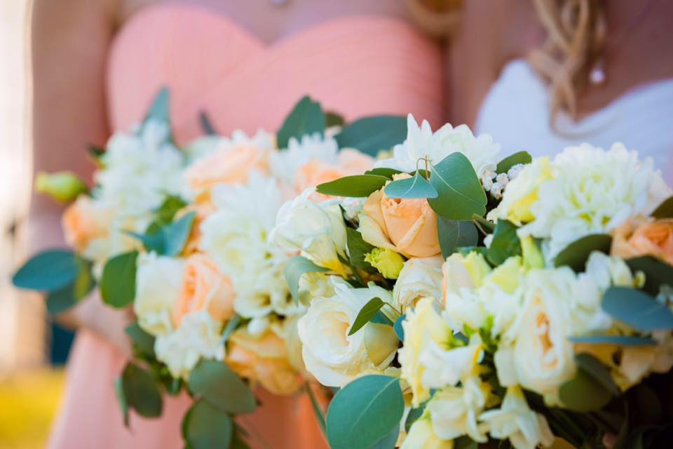 Bridesmaids holding bouquets of peach and white flowers; close up.
