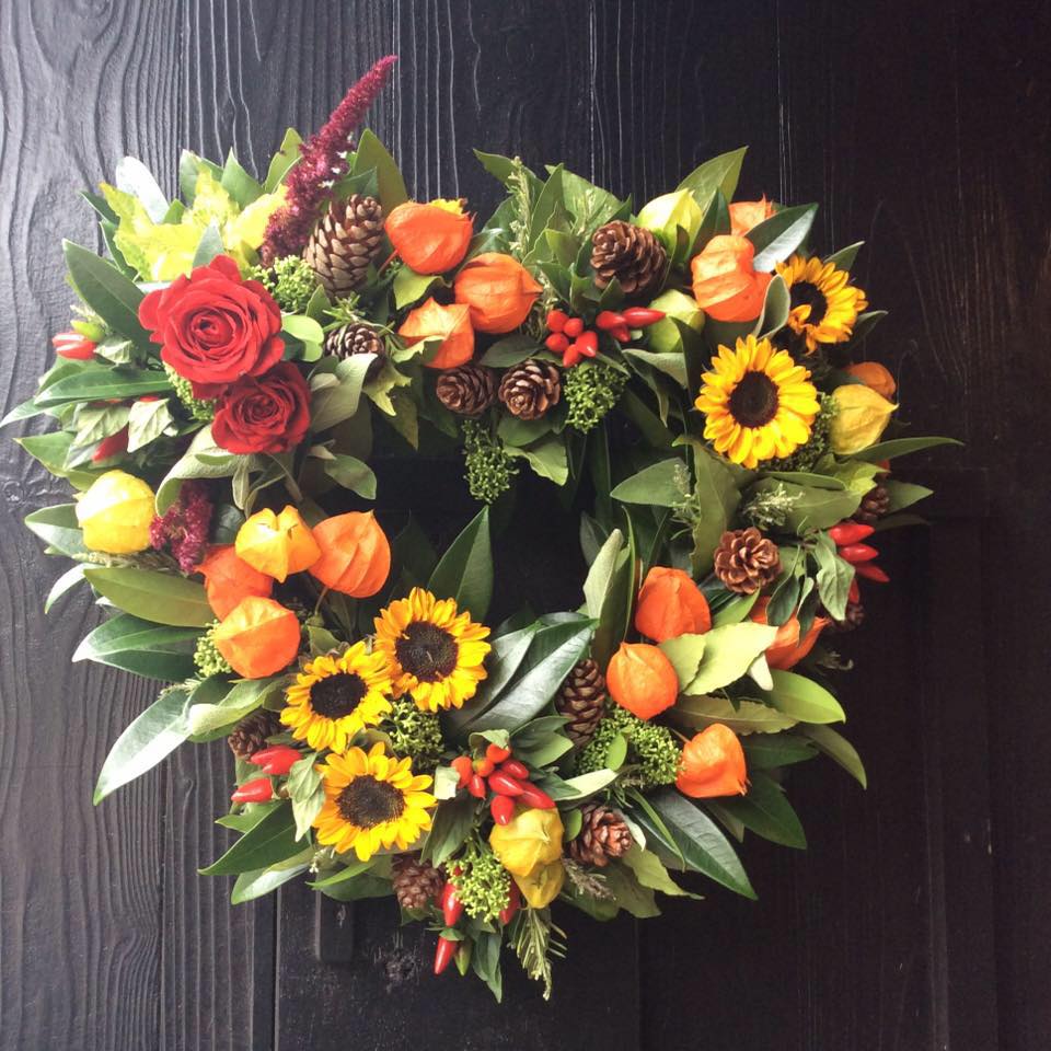 Autumnal wreath with red roses, sunflowers, orange lanterns, and pinecones.