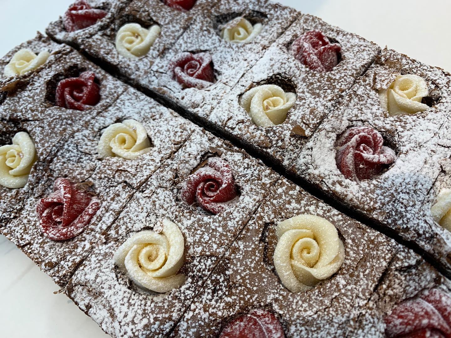 Brownies cut into squares, dusted with powdered sugar, and decorated with white and red buttercream roses.