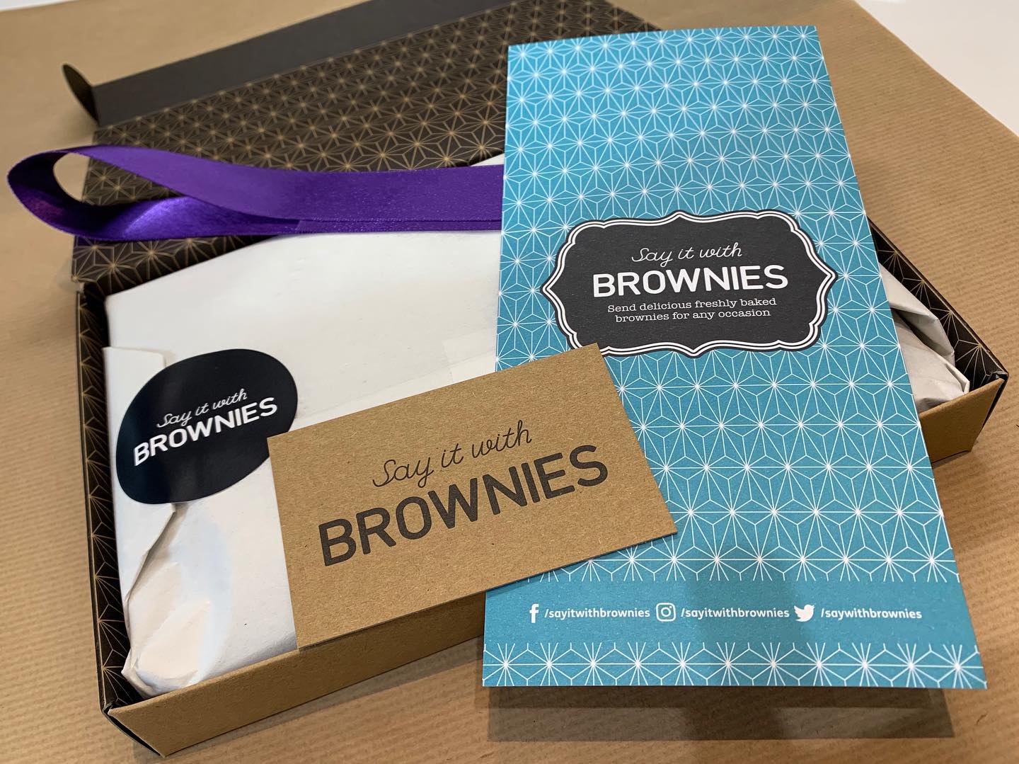 Brownie gift box with purple ribbon, a card, and a patterned sleeve.