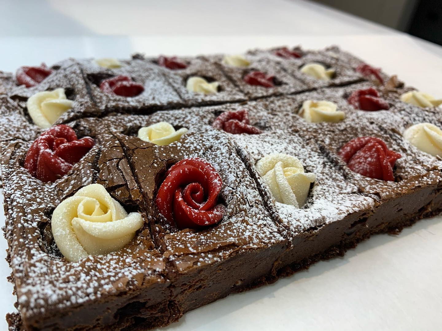 Brownies cut into squares, decorated with red and white frosting roses, dusted with powdered sugar.
