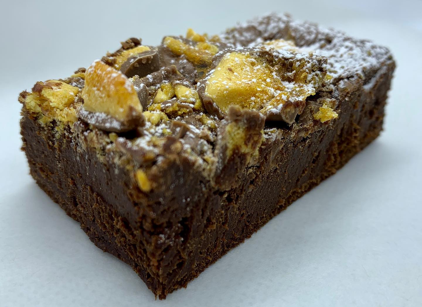 Chocolate brownie topped with honeycomb and powdered sugar on a white surface.