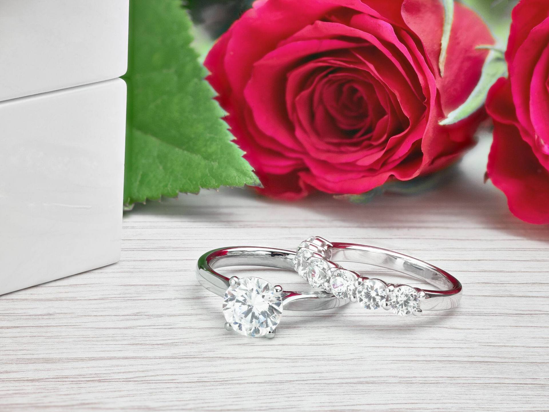Two diamond rings, red roses, and a white box on a wooden surface.