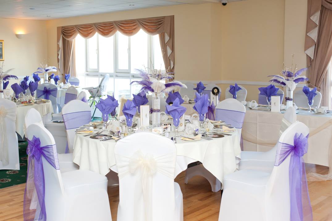 Elegant wedding reception tables with white linens, purple accents, and chair covers.