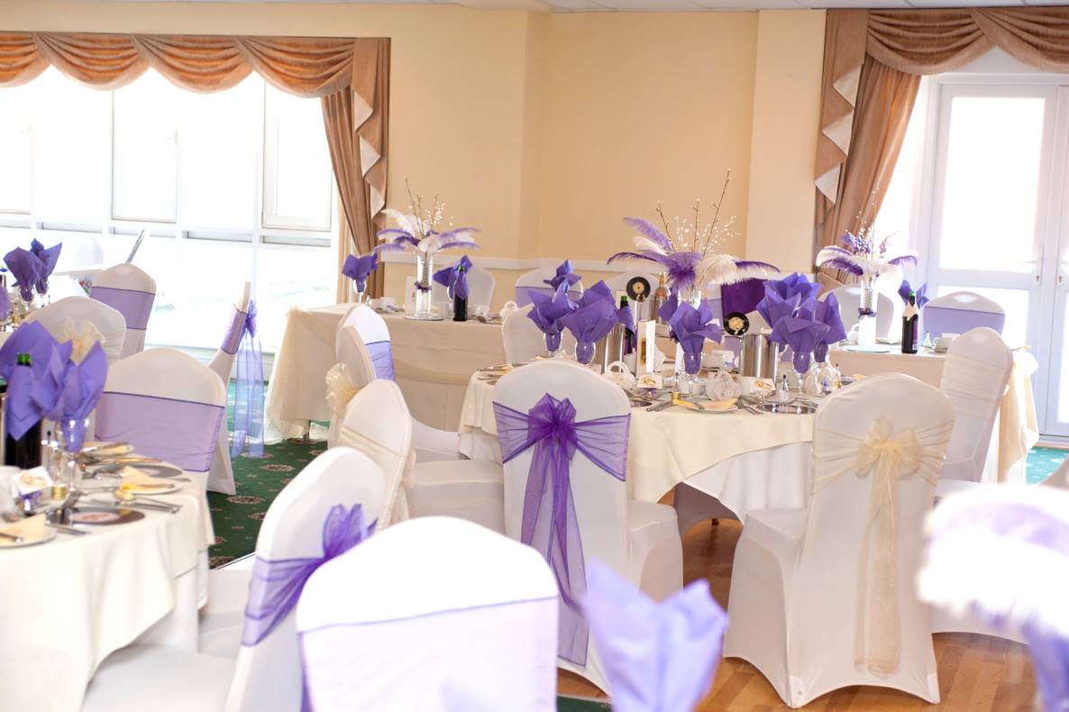 Tables set for a celebration in a room with white and purple decorations.