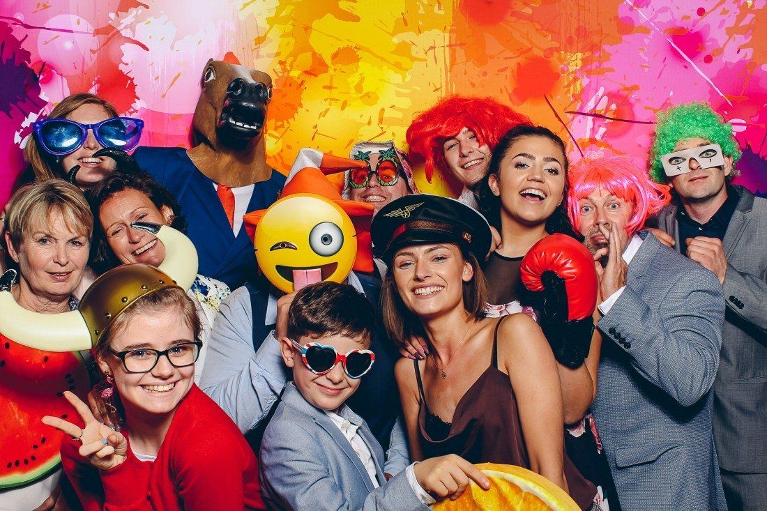 Group of people in costumes and wigs posing for a photo booth with a colorful backdrop.