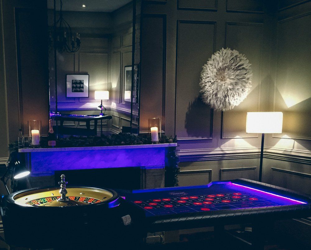Roulette table in a dimly lit room with purple ambient lighting. Candles and a decorative wall hanging are also visible.