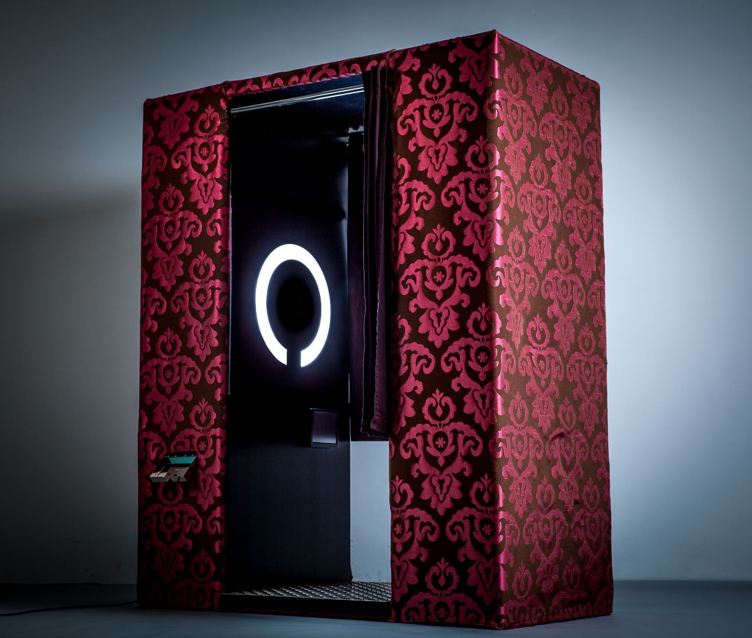 Photo booth with red damask pattern exterior, black interior with circular light, silver base.