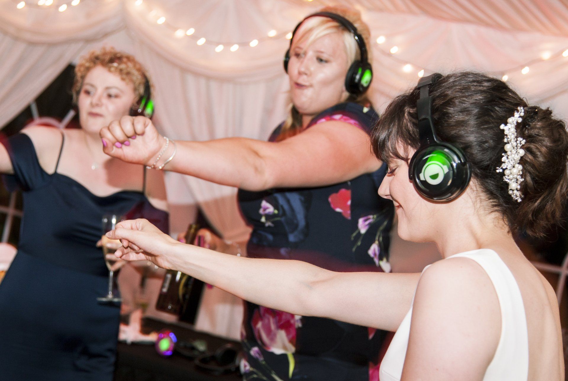 Three women dancing with headphones at a party, illuminated with green lights.