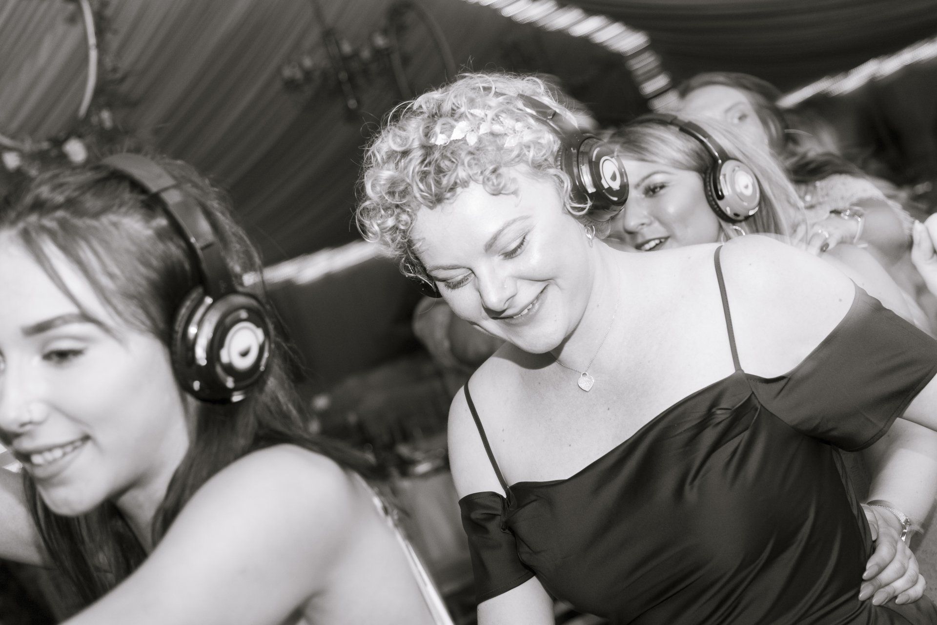People dancing in a party setting, wearing headphones. The woman in the center smiles.