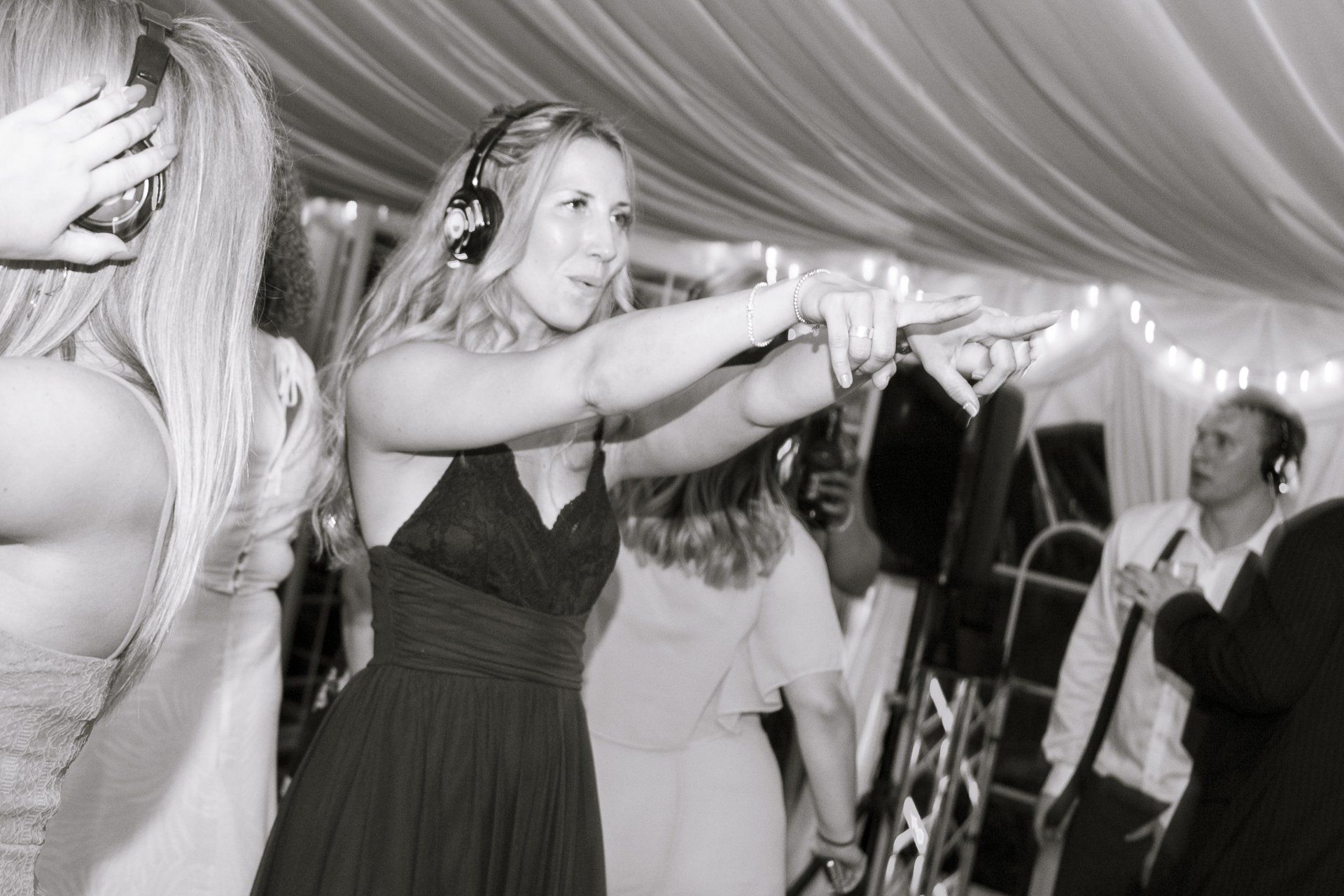 Woman dancing with headphones on, pointing towards the right in a party setting.