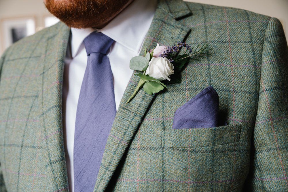 Man in green plaid jacket, lavender tie, pocket square, and boutonniere.