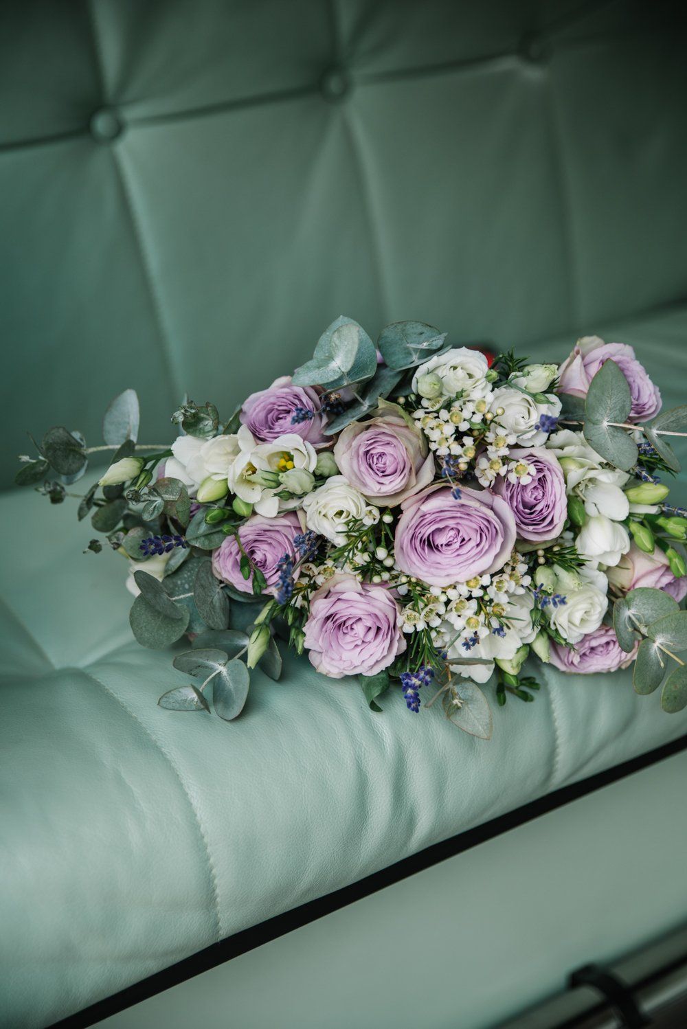 Bouquet of lavender and white flowers on a teal tufted surface.