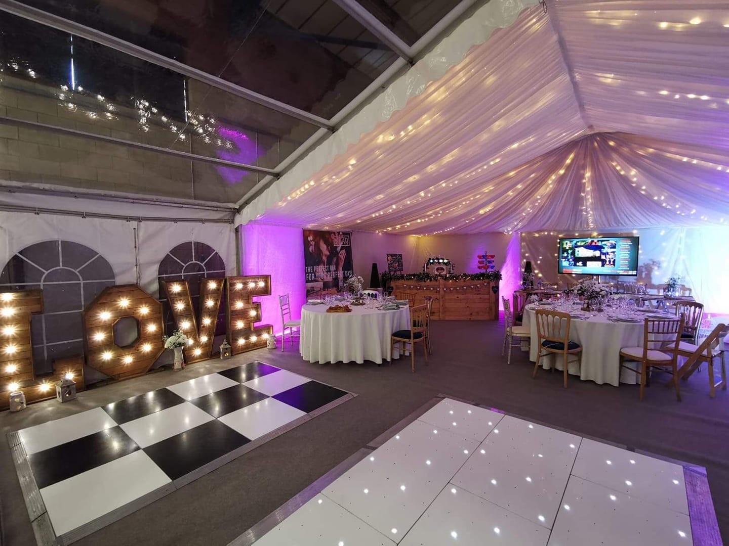 Interior of a wedding reception tent with a dance floor, tables, string lights, and LOVE sign.