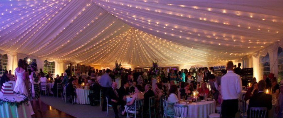 Wedding reception in a tent with string lights and tables set for guests.
