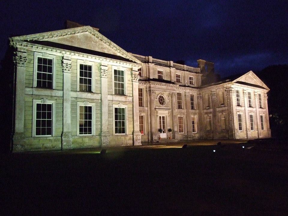 Large, illuminated classical building at night. White facade, symmetrical design, many windows, dark sky.