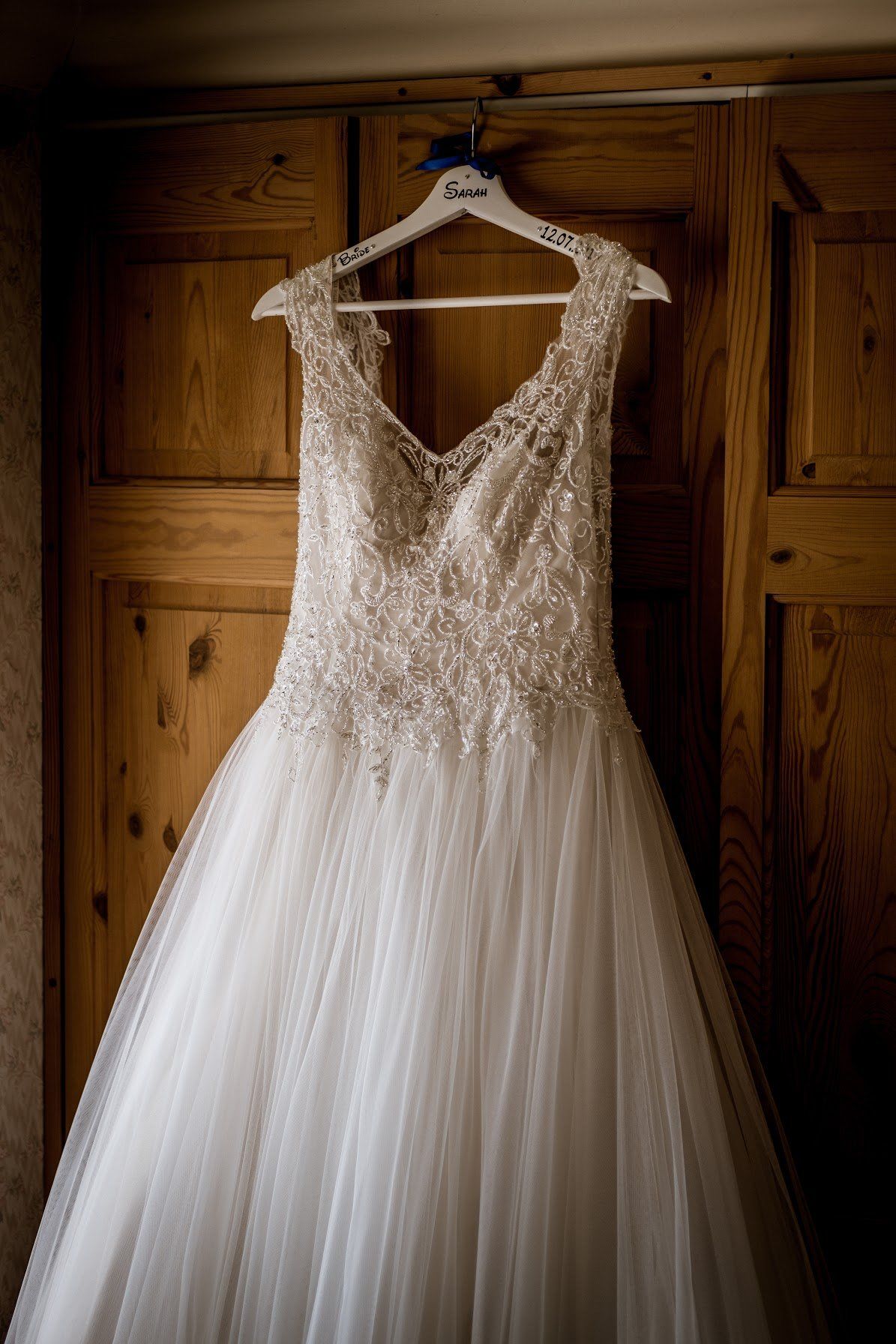 Wedding dress hanging on a wooden closet door; beaded bodice and tulle skirt.