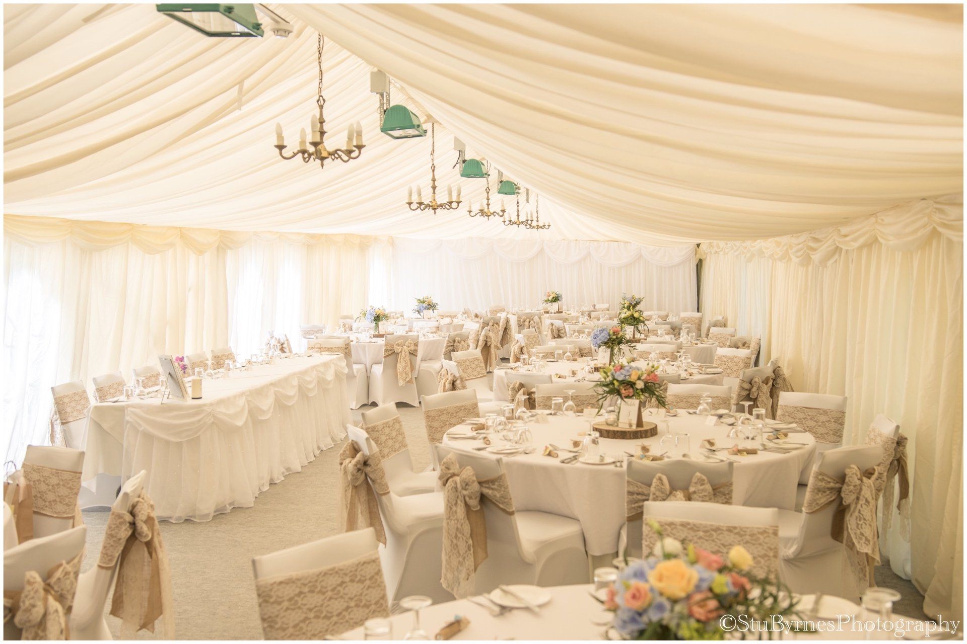 Wedding reception tent, decorated with white linens, floral centerpieces, and covered chairs.