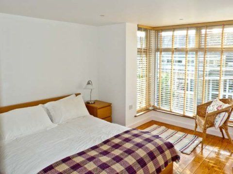 Bedroom with a bed, nightstand, and window seat with blinds. Plaid blanket, and wood flooring.