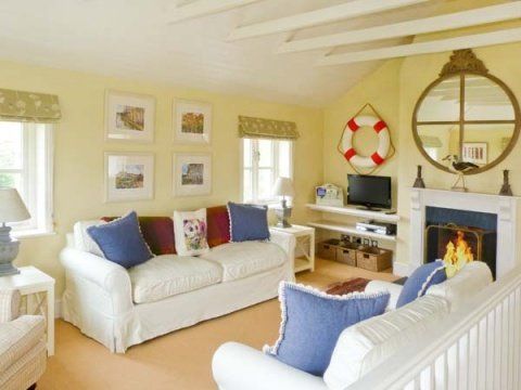 Cozy living room with cream sofa, blue pillows, and fireplace, decorated with nautical accents and framed artwork.