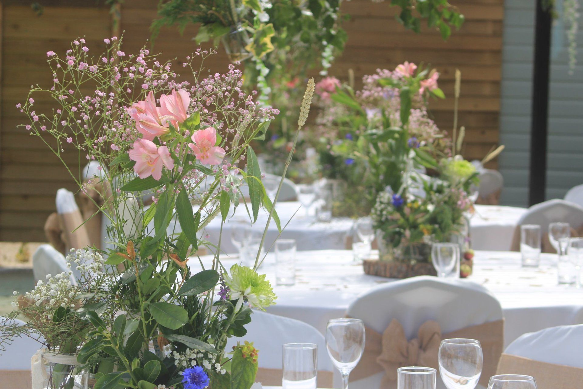 Round tables set for a celebration with floral centerpieces, white tablecloths, and wine glasses.