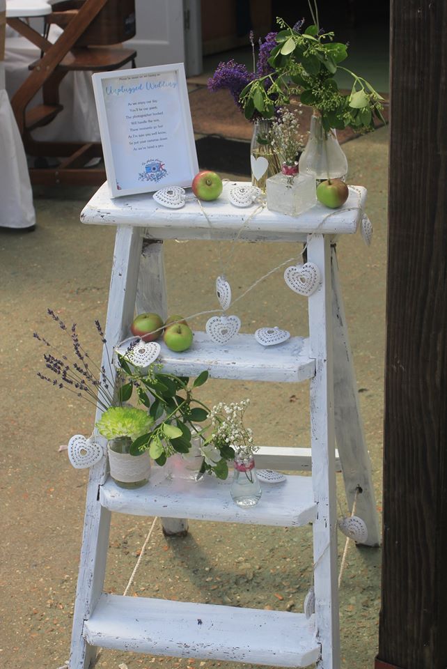 White ladder shelf decorated with apples, flowers, and a framed sign, possibly for a wedding.