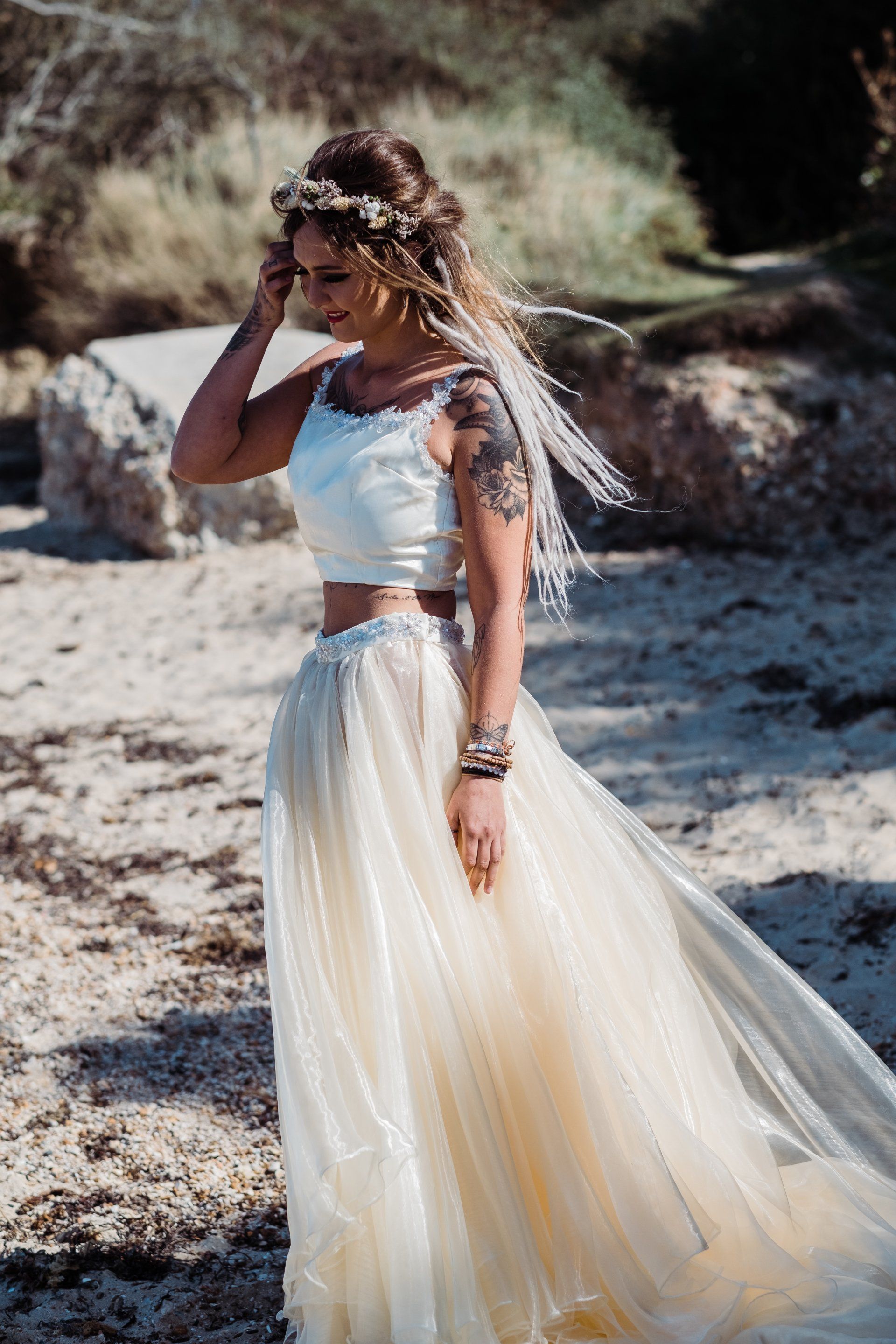 Woman in crop top and tulle skirt, wearing a floral crown, on a beach.