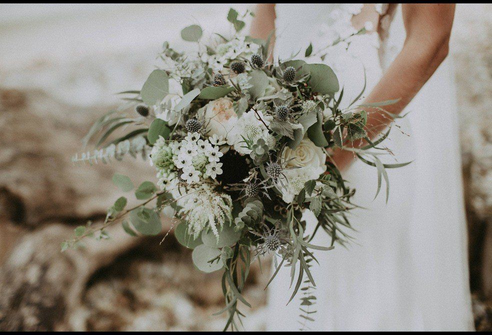 Bride holding a white and green floral bouquet outdoors.
