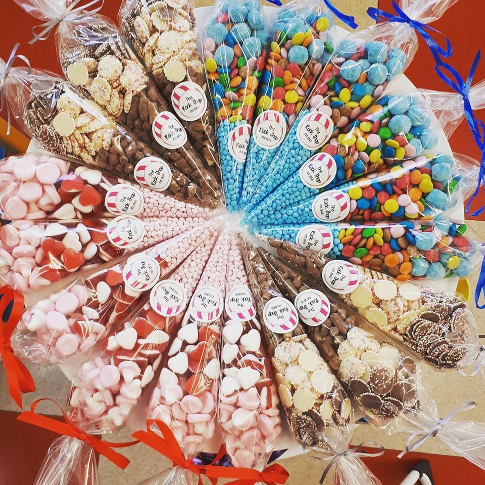 Arrangement of cone-shaped bags filled with various colorful candies tied with ribbons; white and red color scheme.